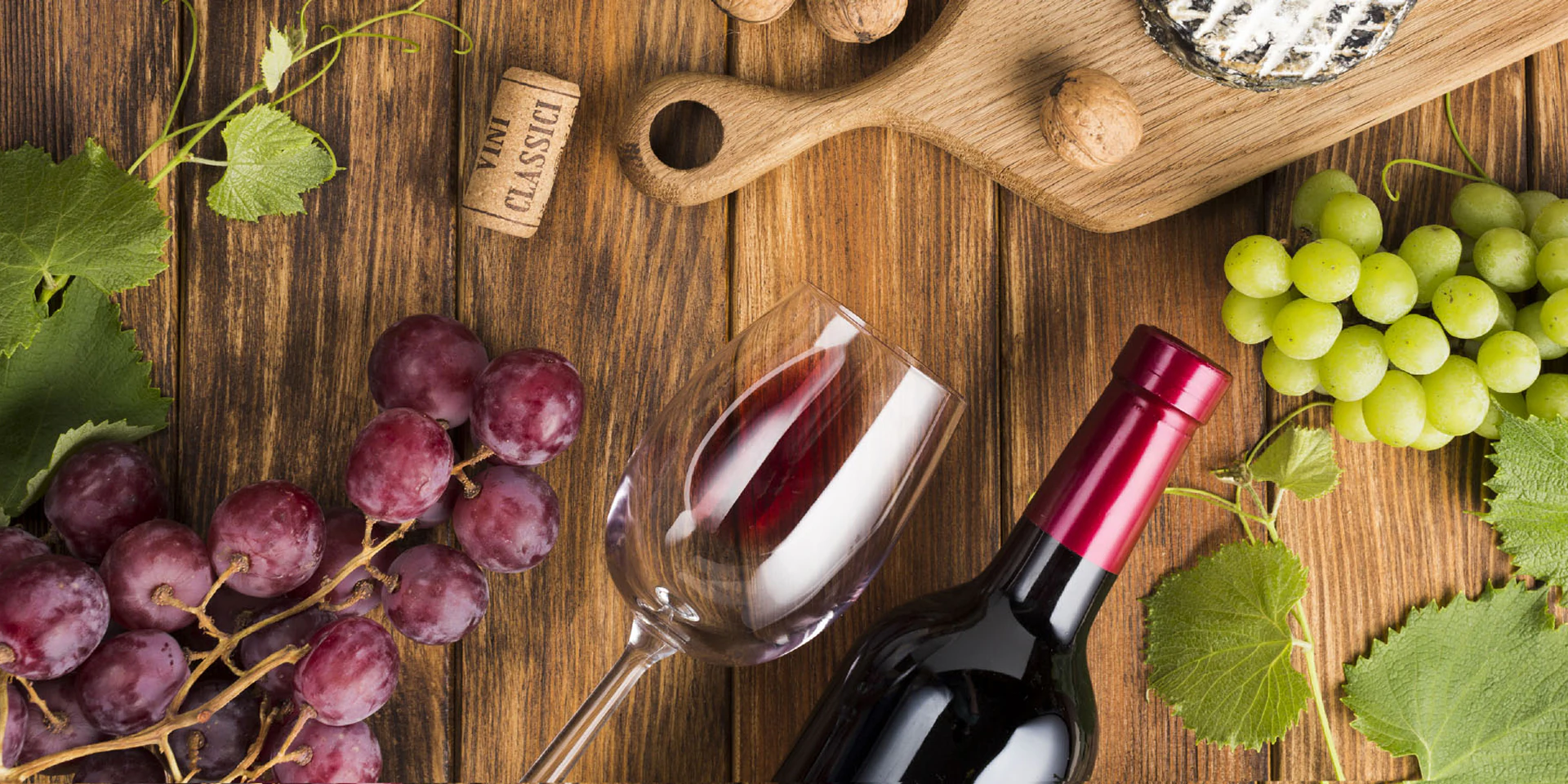 Wine bottle and glass styled with grapes and cheese on a wooden board